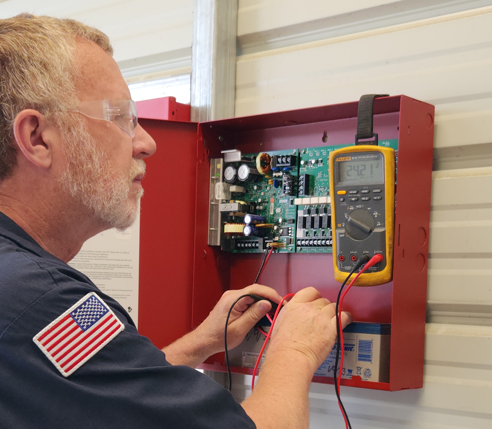 Technician testing a fire alarm control panel with a multimeter in the field